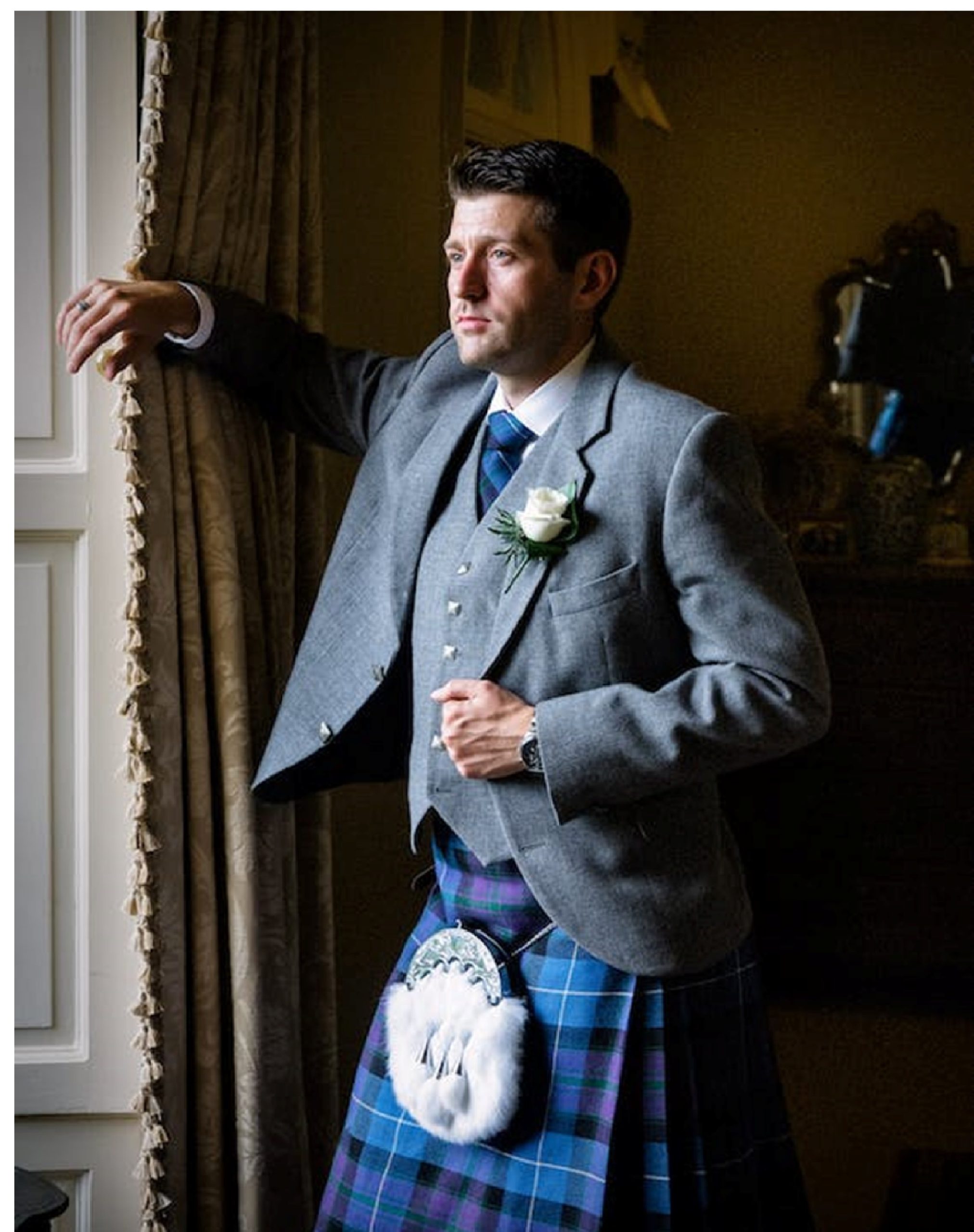 men wearing silver coat with formal kilt. standing beside of window.