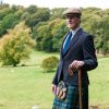 man wearing Scottish kilt and sporran standing on meadow leaning on cane looking at camera