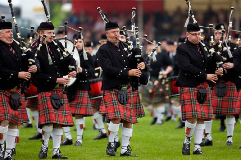 Men wearing vibrant red Scottish kilts, marching proudly in traditional Highland Games held each year in Dunoon in Scotland.The blurred background adds a dynamic touch, capturing the energy and camaraderie of the moment. Experience the cultural richness and tradition as this group showcases the timeless allure of Scottish kilts.