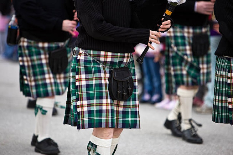 Men marching in a parade wearing Scottish kilt.