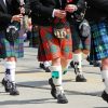 Captured from a low angle, this striking image showcases four individuals wearing kilts in various vibrant colors, marching with purpose. The kilts, reminiscent of both Scottish and Irish traditions, add a colorful and cultural flair to the scene. Witness the harmony of different hues as these individuals proudly showcase their heritage and the timeless appeal of kilts.